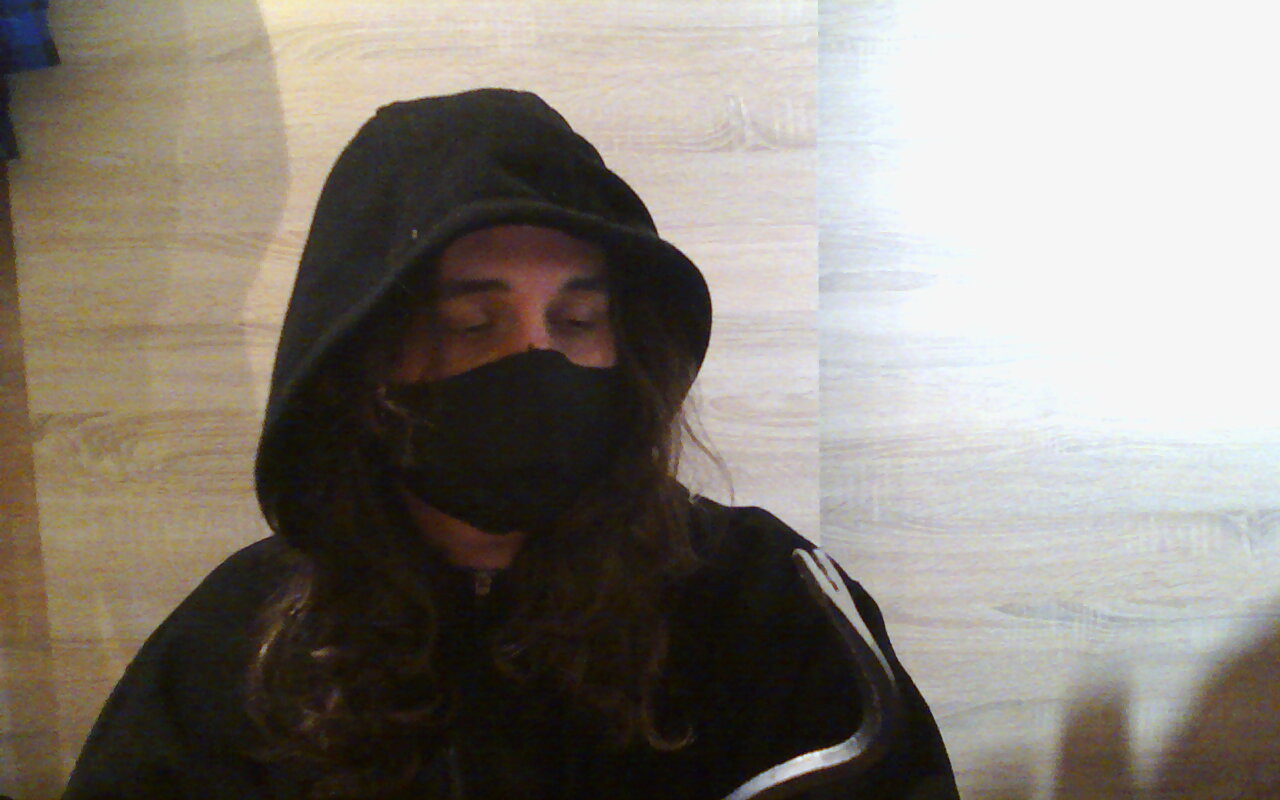 webcam photo of me wearing a black hoodie and a black face mask, looking down at the curved end of a crowbar contemplatively 