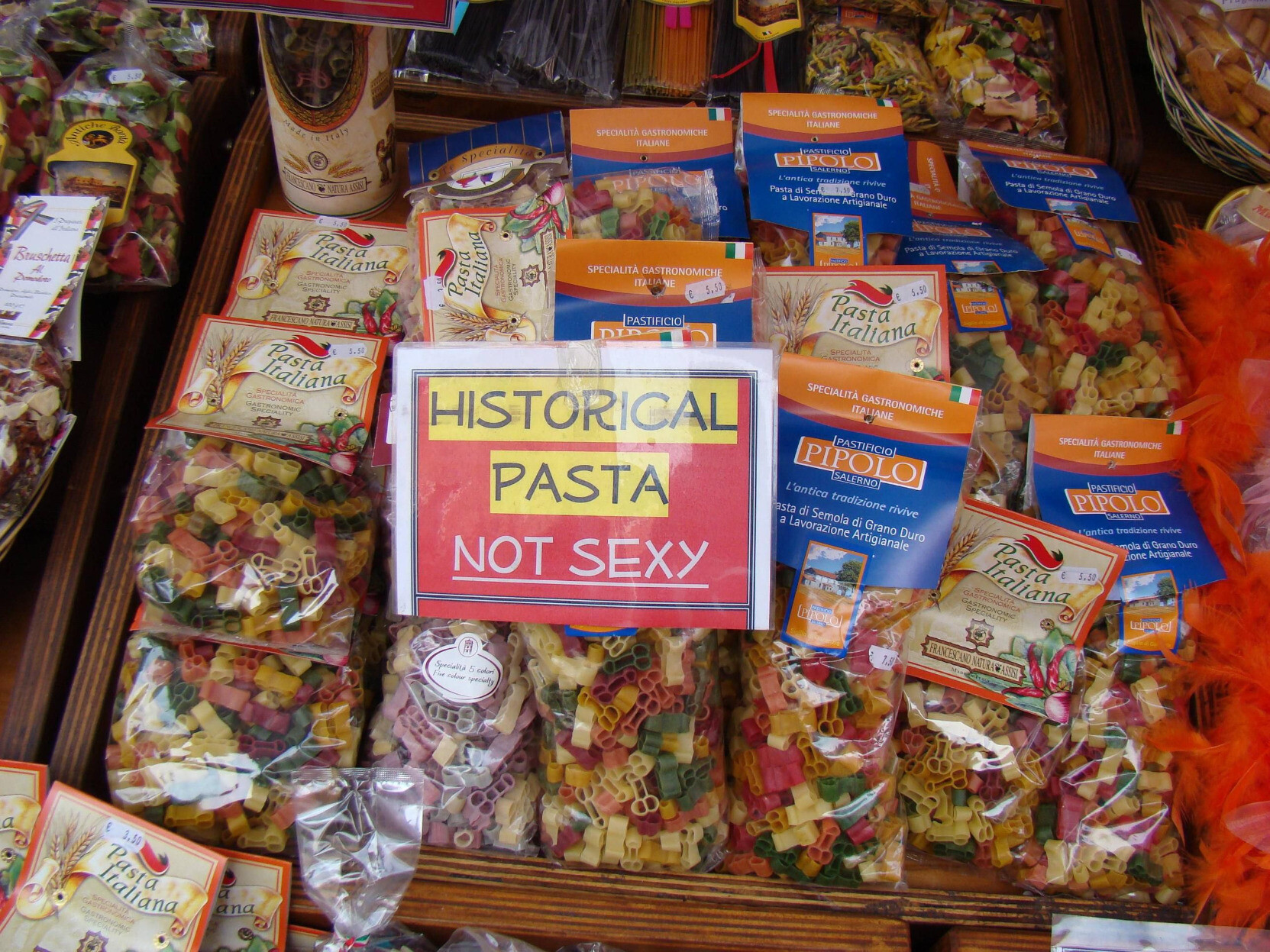 A store shelf with a sign that says "HISTORICAL PASTA - NOT SEXY" 
The shelf is filled with several bags of red, green and yellow pasta that is shaped like dicks. They're cocks. There's no way they're anything but penises