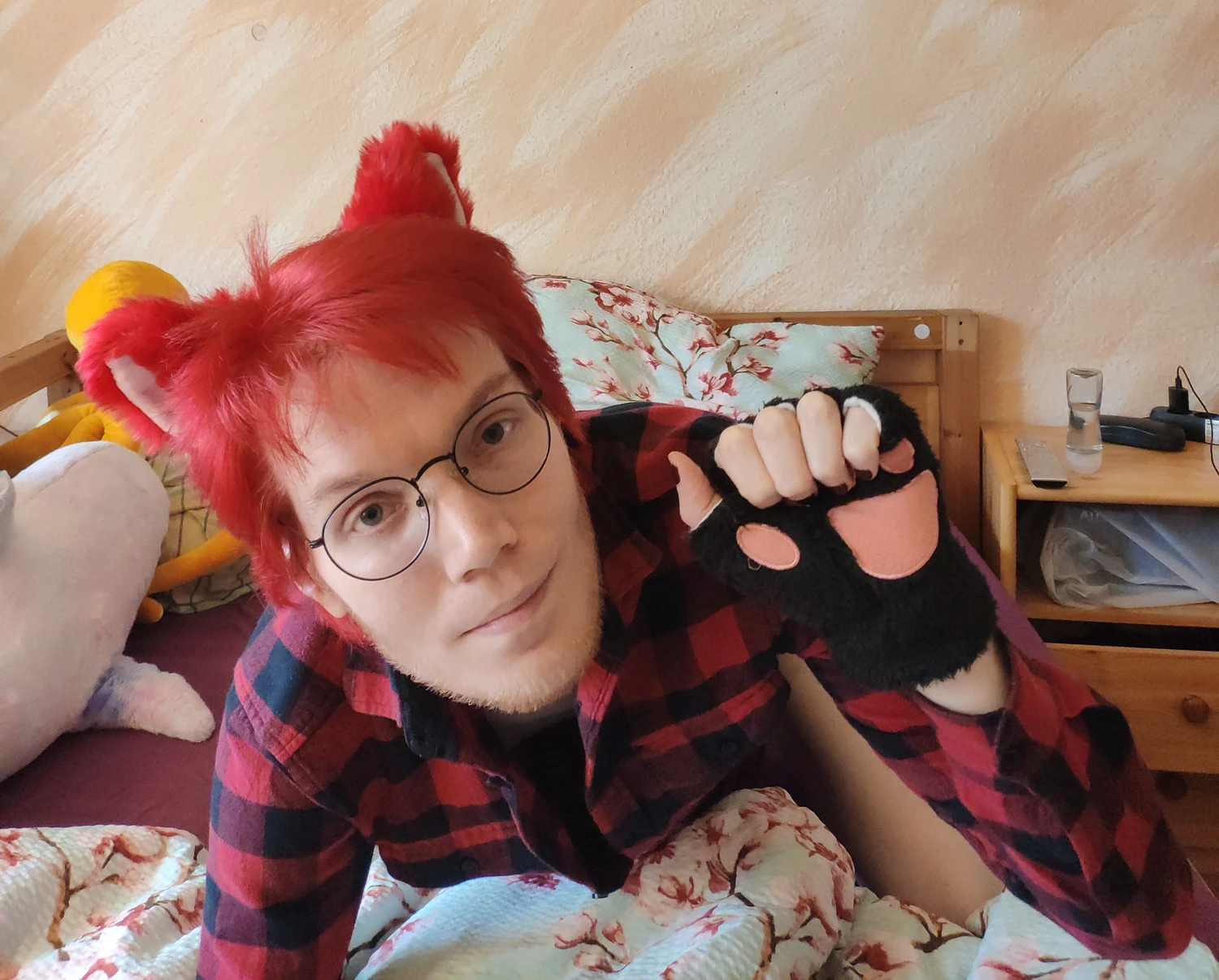 me in a bed, on all fours, looking at you. i'm wearing red hair and cat ears, big round glasses, a red and black flannel shirt and cat paw gloves. it looks as if i'm meowing.