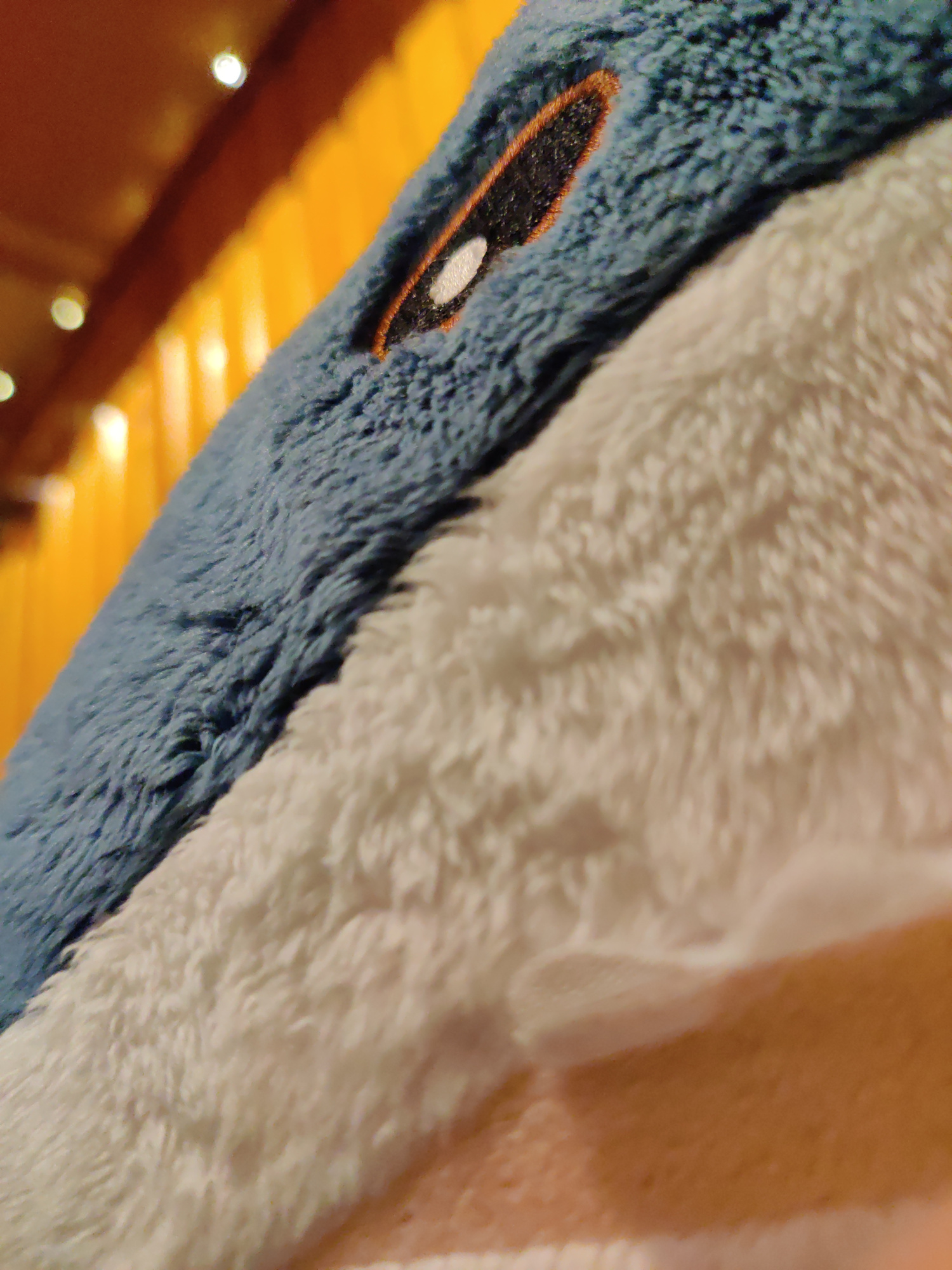 a shark plushie shot from a very short distance, filling most of the frame. its eye and some of the mouth is visible. there are blurry fairy lights in the background.