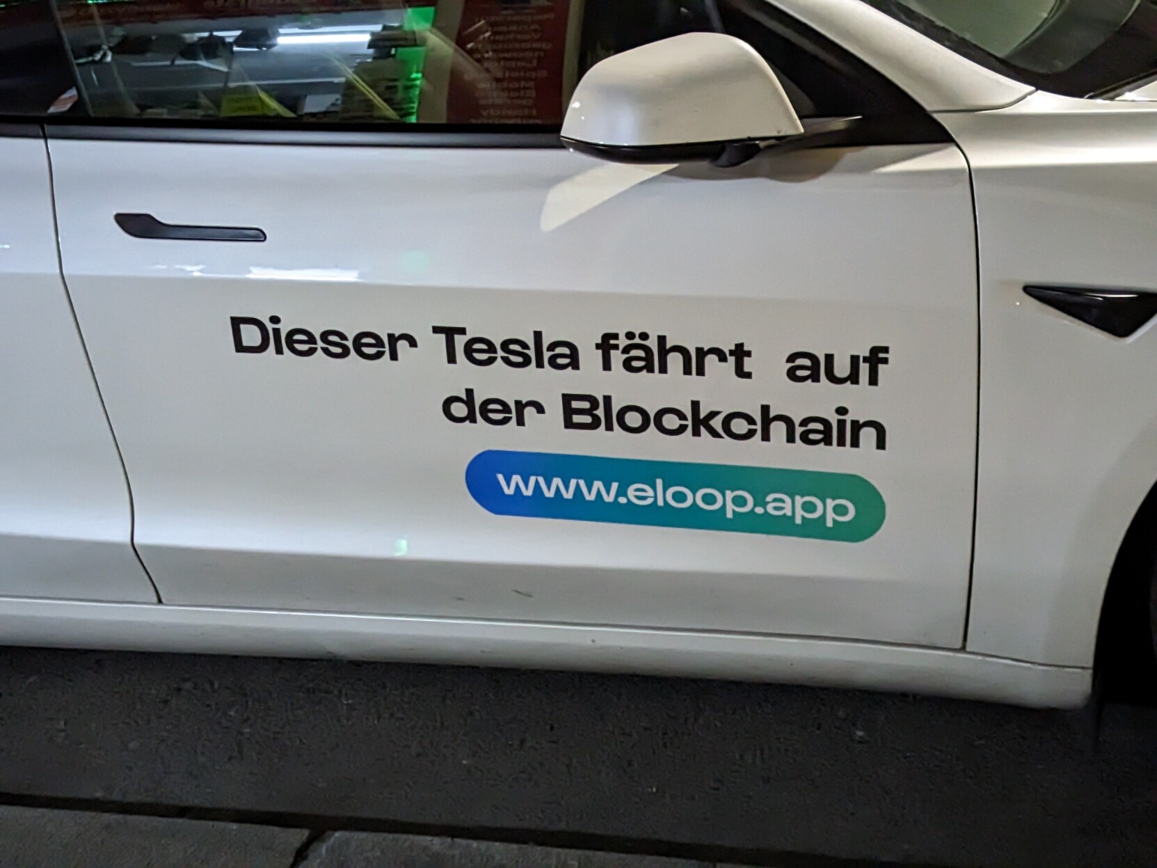 text on side of eLoop car: the blockchain drives this tesla (dieser tesla fährt auf der blockchain)