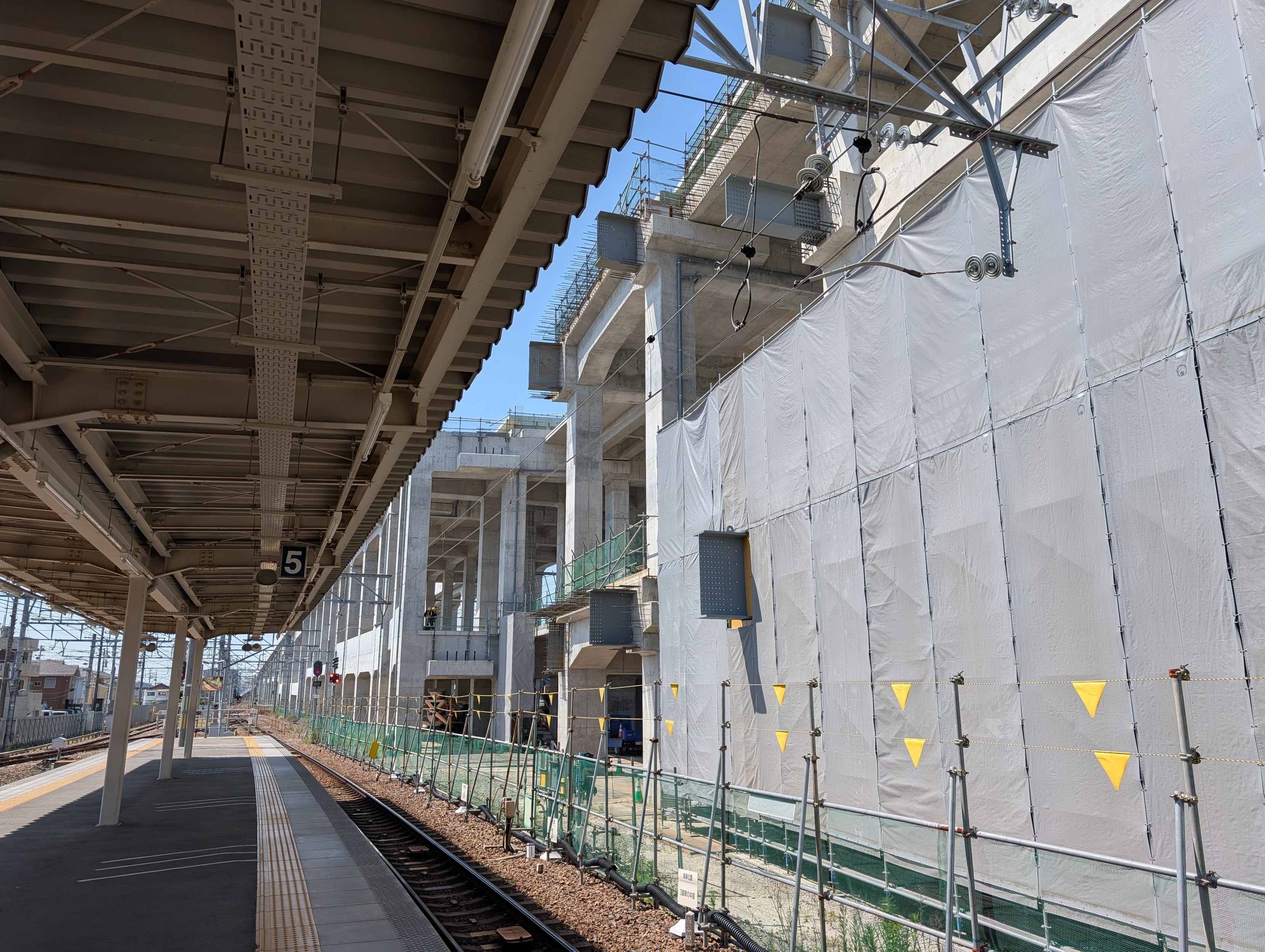 Looking at the worksite from the side from an adjacent platform canopy. There's a substantial fence between the live railway and the worksite. 

Some large steel structural beams extend out the site, but it's mostly still a concrete shell. 