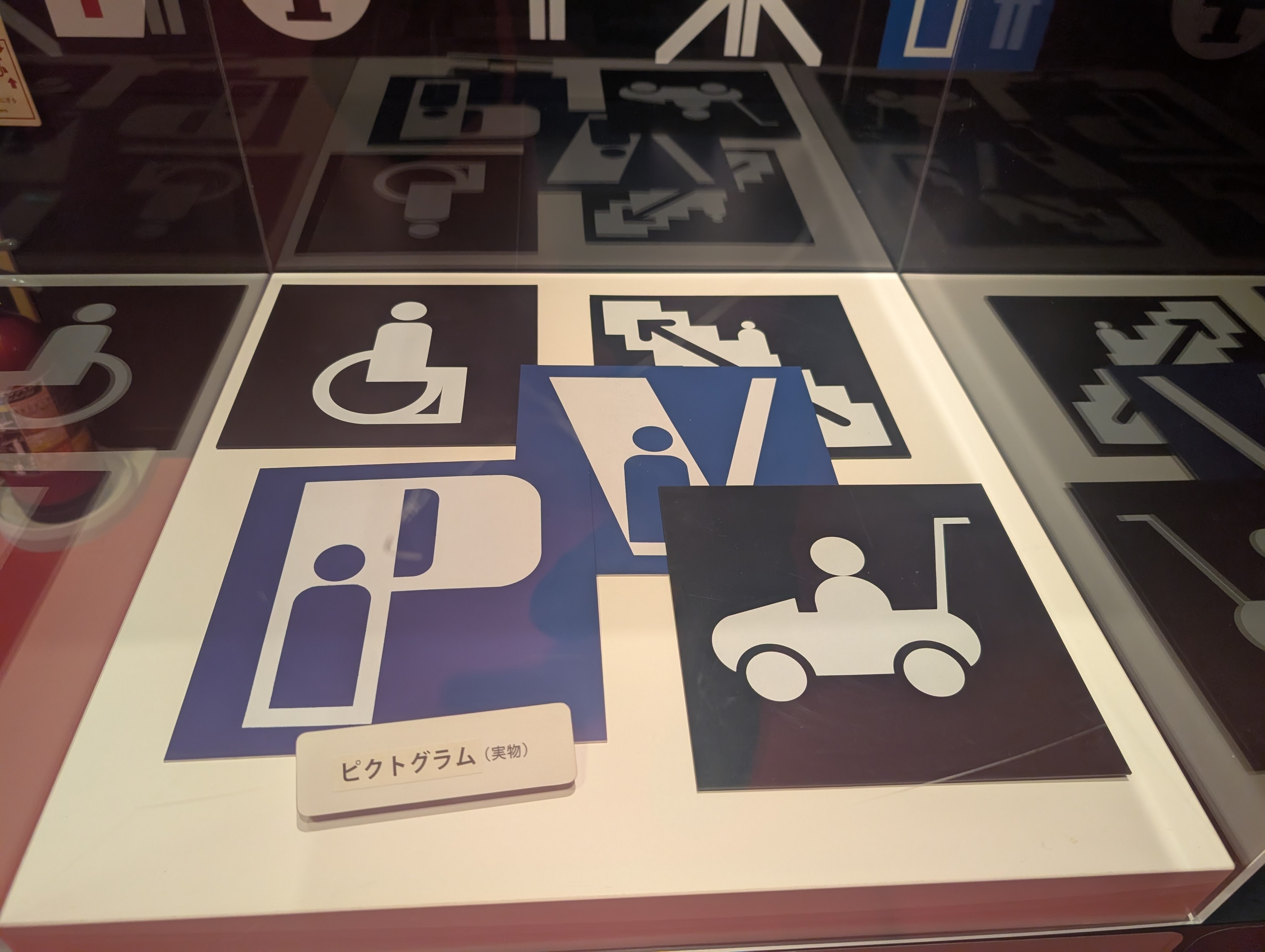 A selection of icons in a display case, from top right to bottom left: 
- disabled 
- staircase? escalator? 
- P with a person? 
- V with a person? 
- prams 