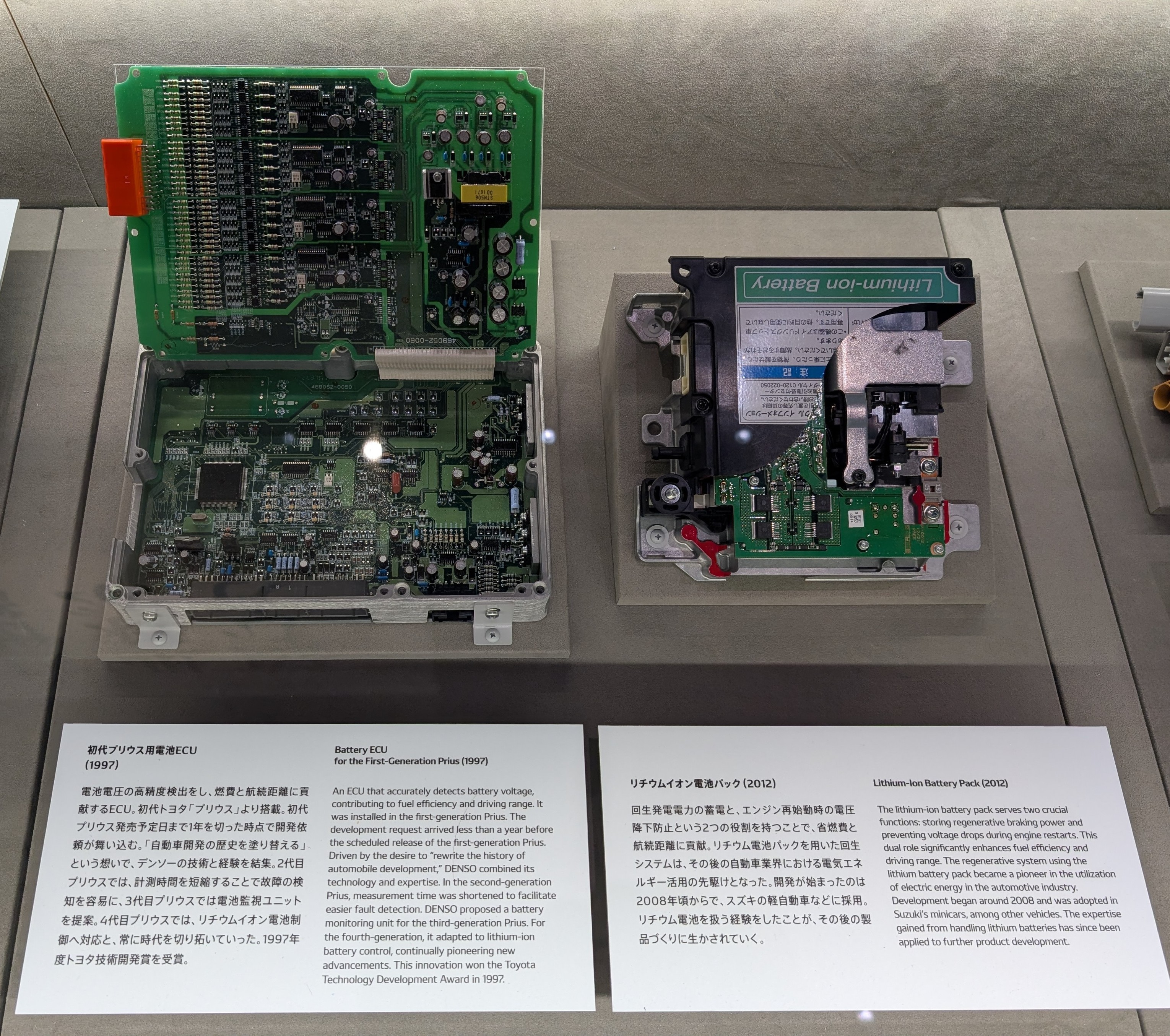 A DENSO BMS and battery. The placards read (truncated): 

Battery ECU the First Generation Prius (1997)

ECU that detects battery voltage contributing to fuel efficiency and driving range was installed in the fest-generation Prius. The development request arrived less than a year before. 

Lithium-Ion Battery Pack (2012)

The battery pack functions, storing regenerative braking power and preventing vintage drops during engine restarts. This chuu nike significantly enhances fuel efficiency and driving range.