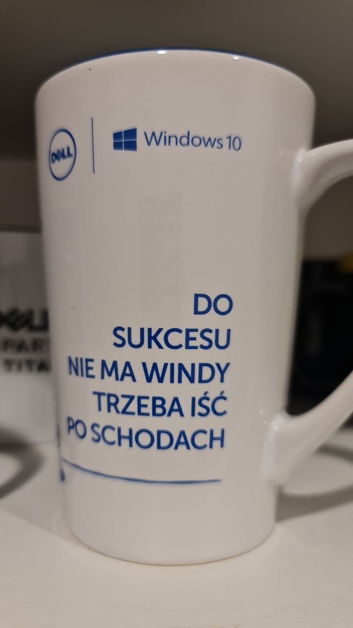 Photo of a white mug. The mug has a Dell logo, Windows 10 logo, and a marketing slogan in Polish, as explained in the main post. Photo of a white mug. The mug has a Dell logo, Windows 10 logo, and a marketing slogan in Polish, as explained in the main post.