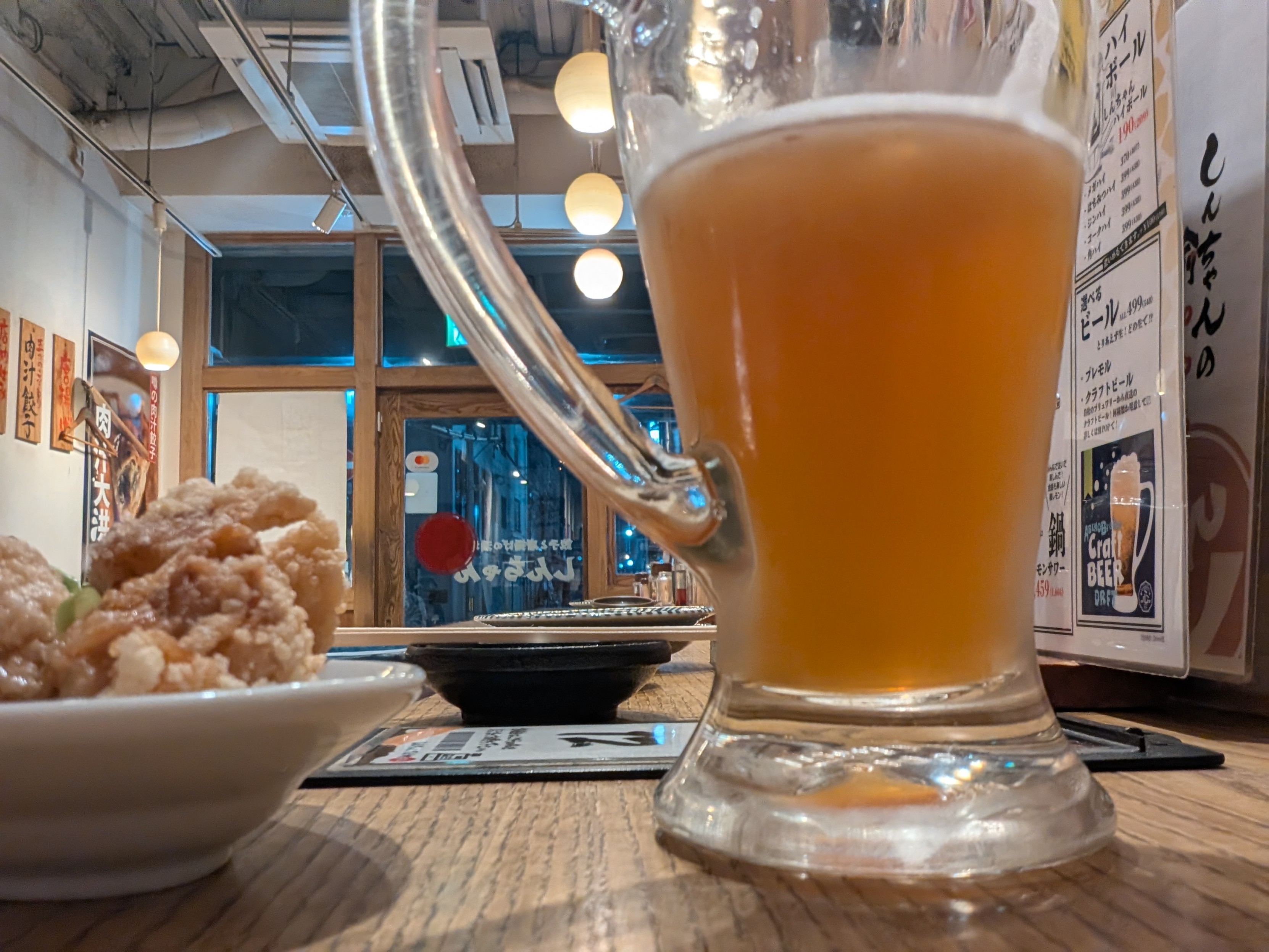 Looking down a bar from a weird angle. A glass of beer dominates, with some fried chicken to the left 