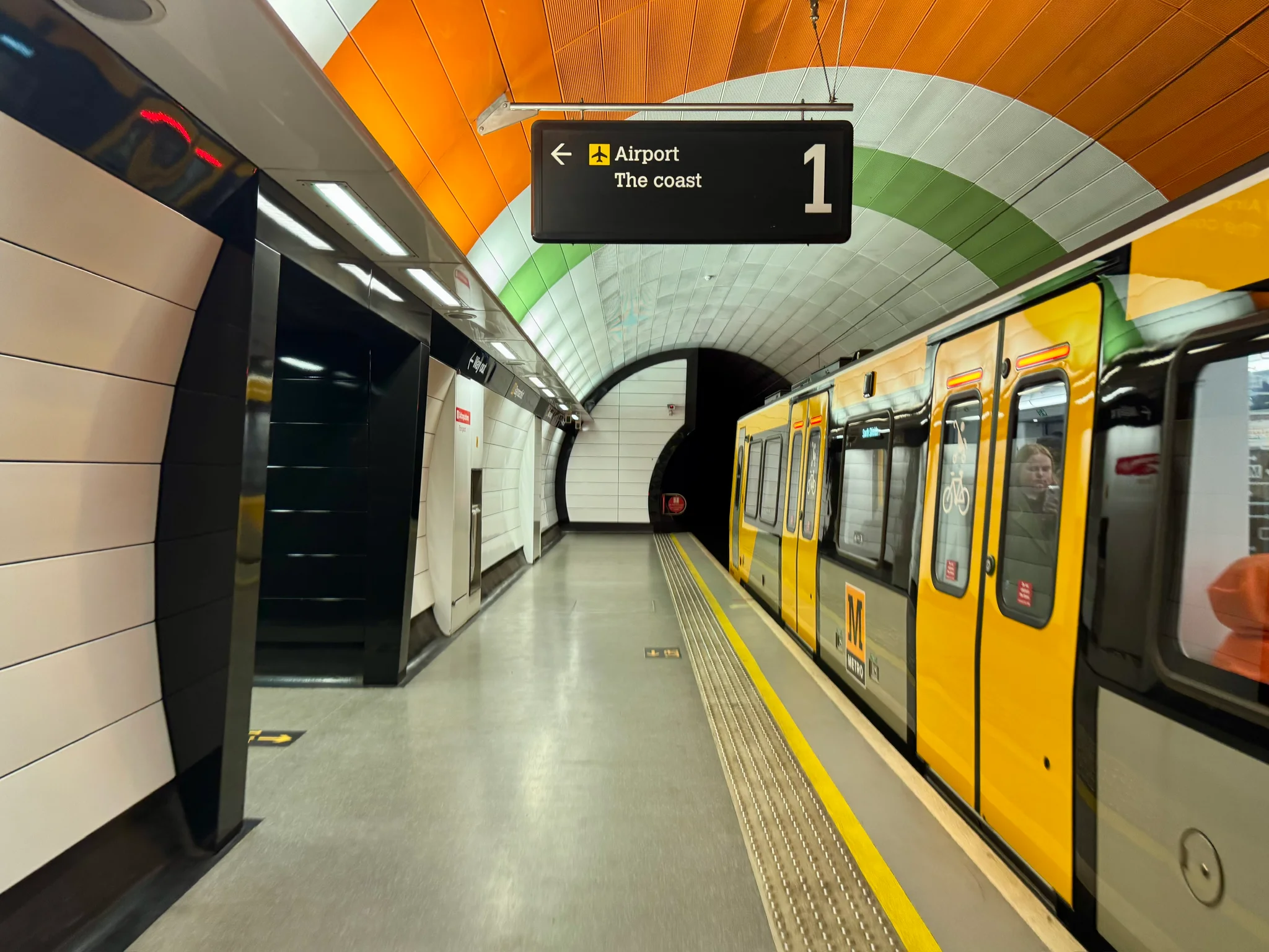A vehicle at the underground Haymarket station. The round ceiling of the station is coloured in white, orange, and green bands.