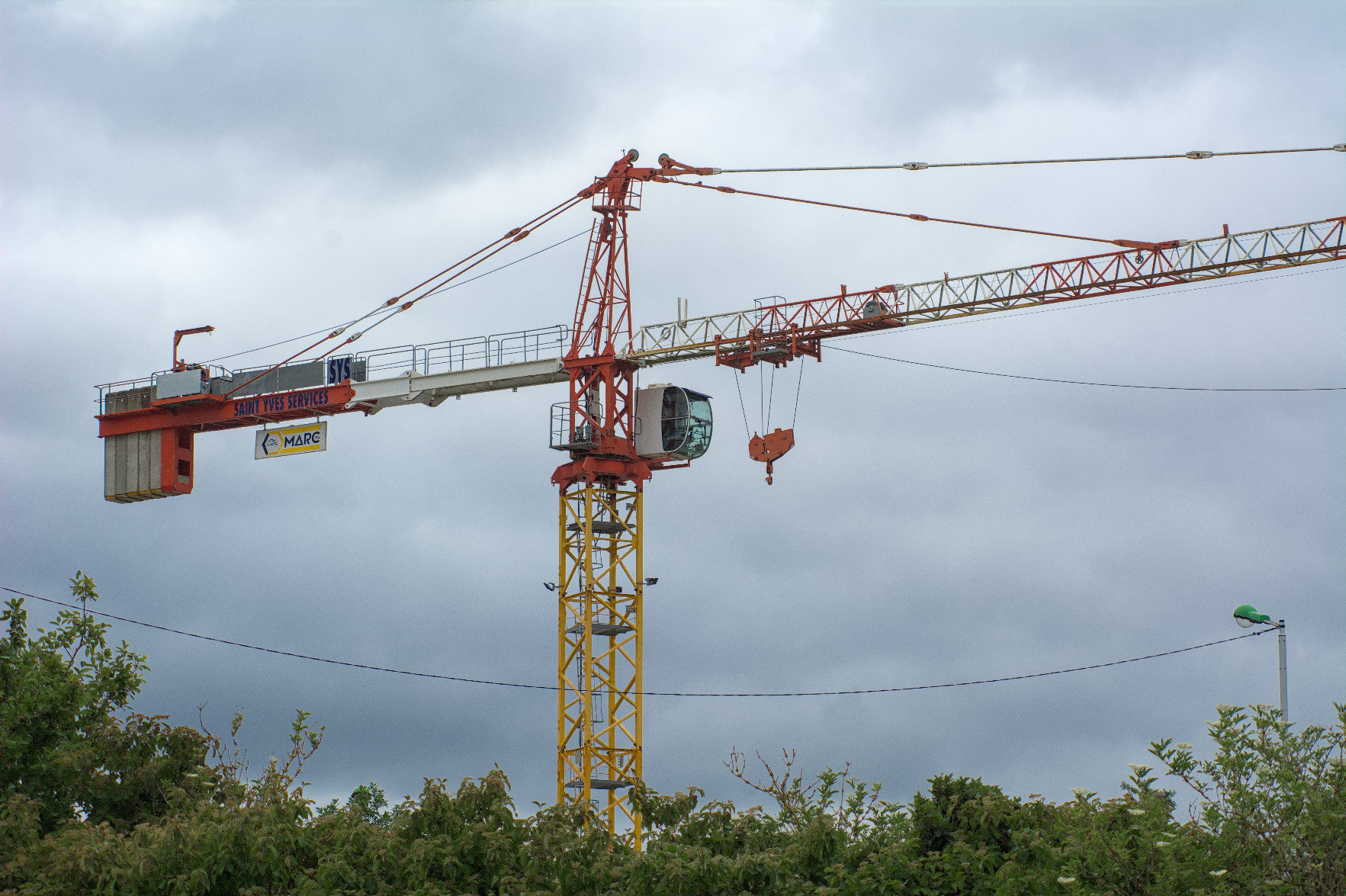 An orange and red crane towering above trees in the cloudy sky. It is unmanned at the moment. An orange and red crane towering above trees in the cloudy sky. It is unmanned at the moment.