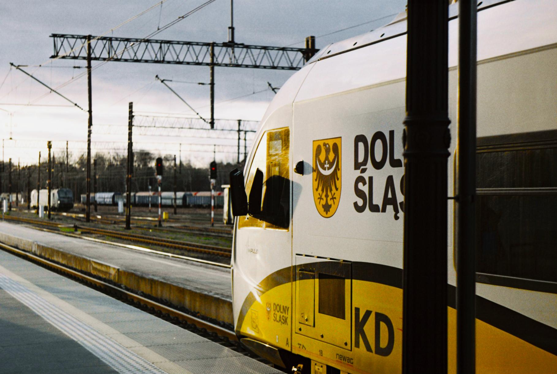 the cab of a yellow, white and black KD train reflecting the low afternoon sun whilst stopped at the platform