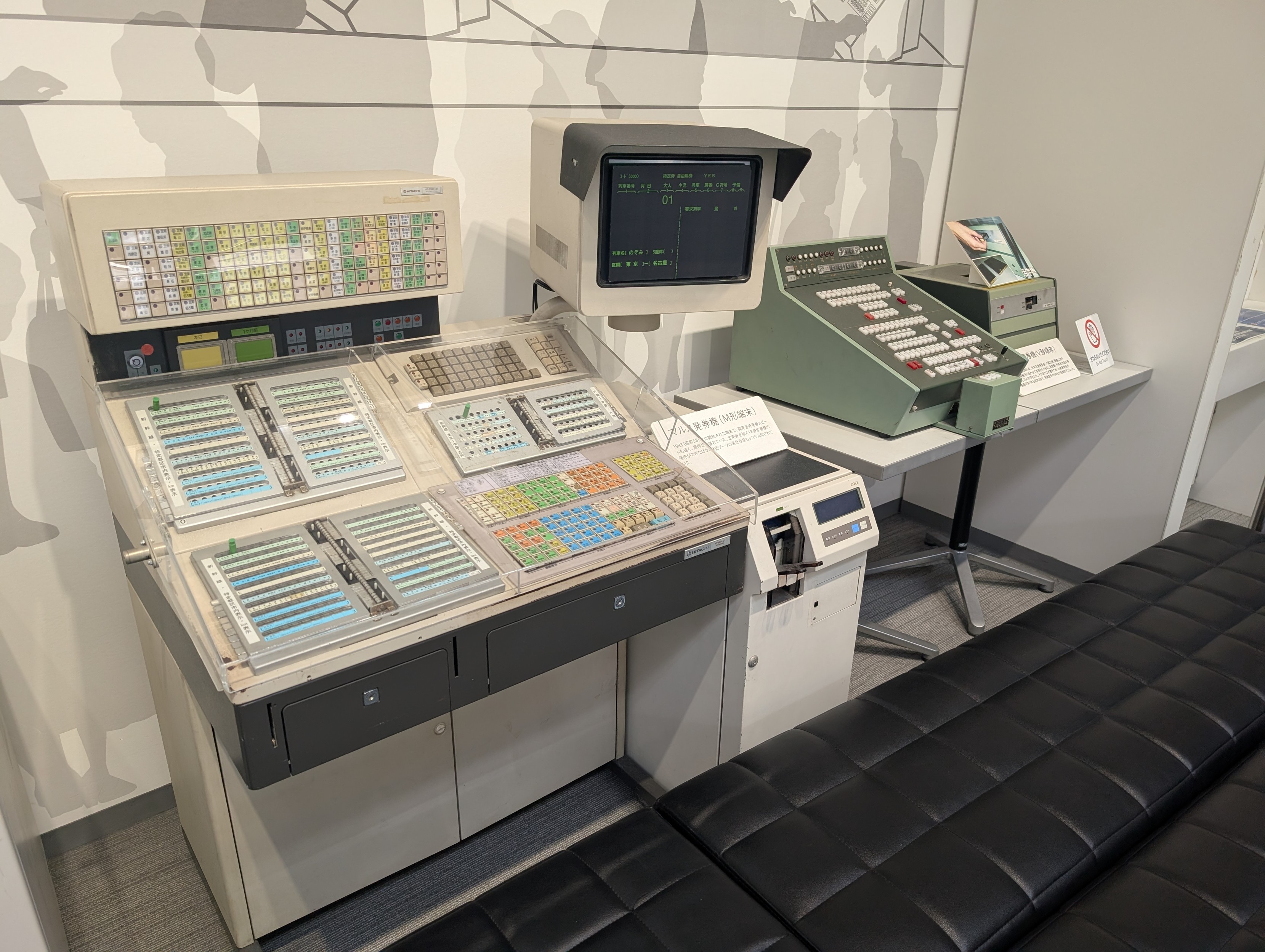 A large computer workstation from the 80s with a very very large application spefici keyboard (Japanese) and a CRT kinda to the side. If you look closely, you can see a ticket printer below. 

https://ja.wikipedia.org/wiki/%E3%83%9E%E3%83%AB%E3%82%B9_(%E3%82%B7%E3%82%B9%E3%83%86%E3%83%A0)