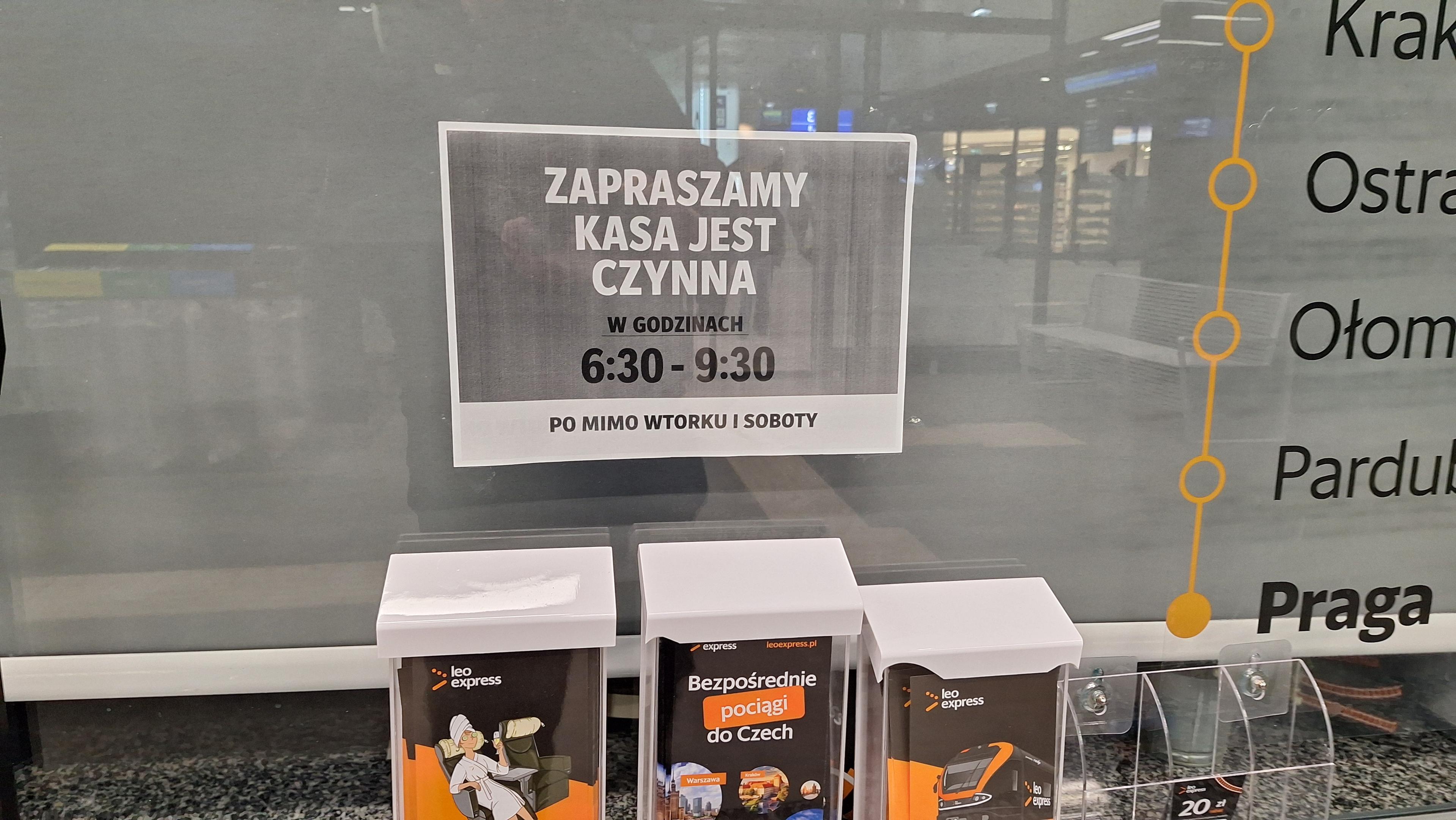 Zamknięta kasa biletowa. Na środku szyby czarno-biała kartka o treści: Zapraszamy, kasa jest czynna w godzinach 6:30-9:30 po mimo wtorku i soboty