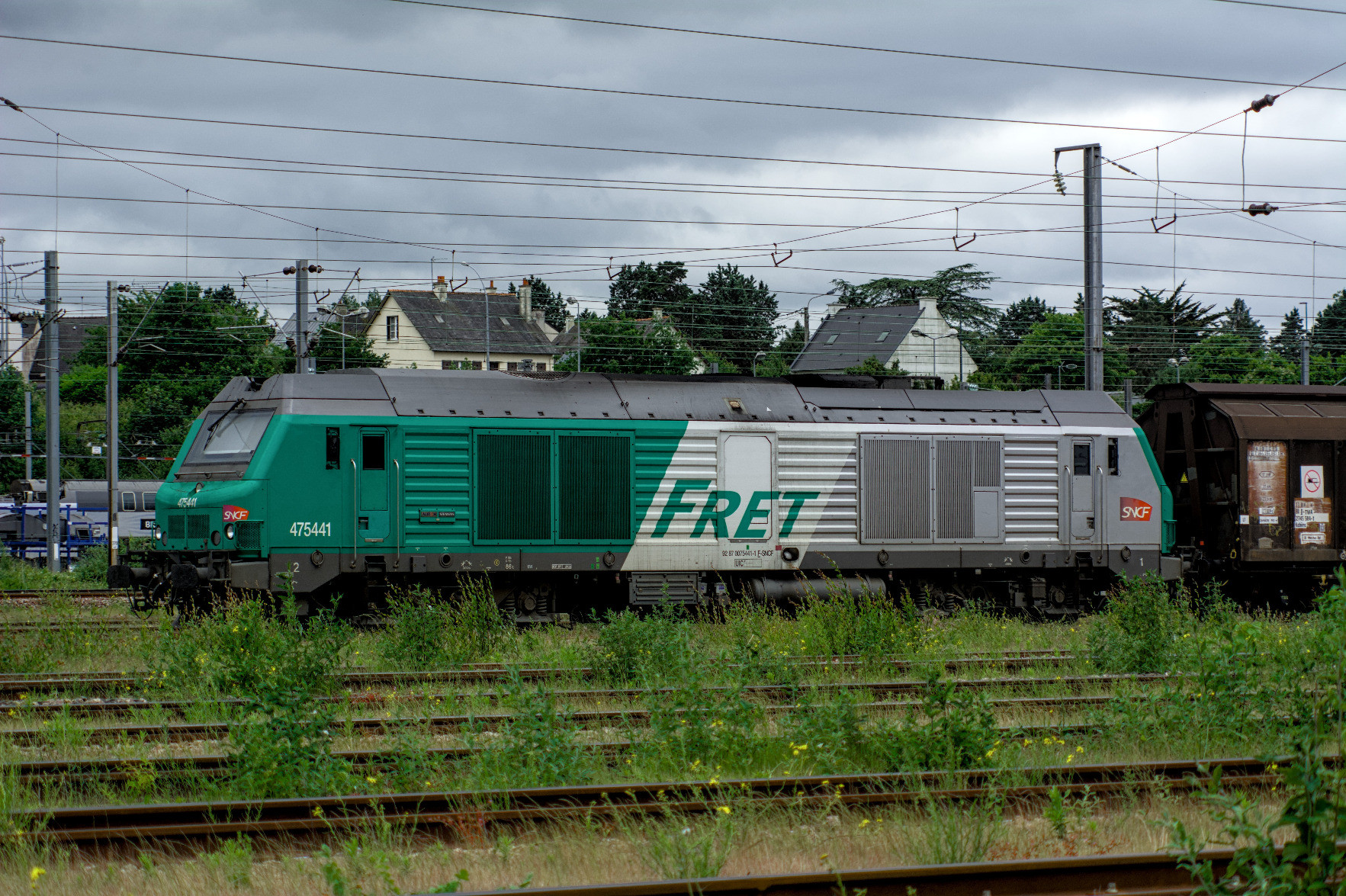 A green SNCF fret locomotive parked in the rail yard; there is a lot of shrubs in the rails in front of it. A green SNCF fret locomotive parked in the rail yard; there is a lot of shrubs in the rails in front of it.