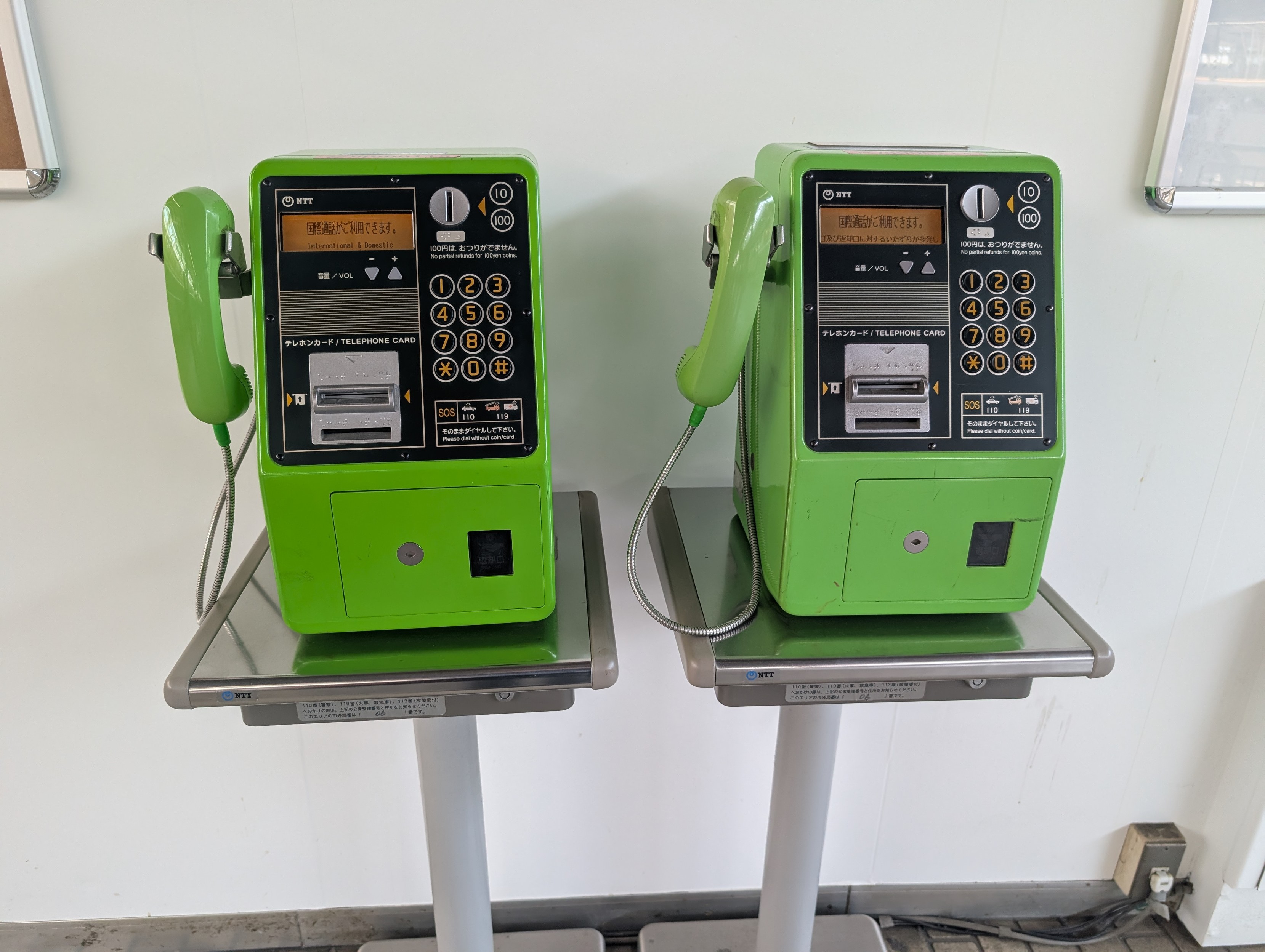 Two green NTT telephones on pedestals, side by side 