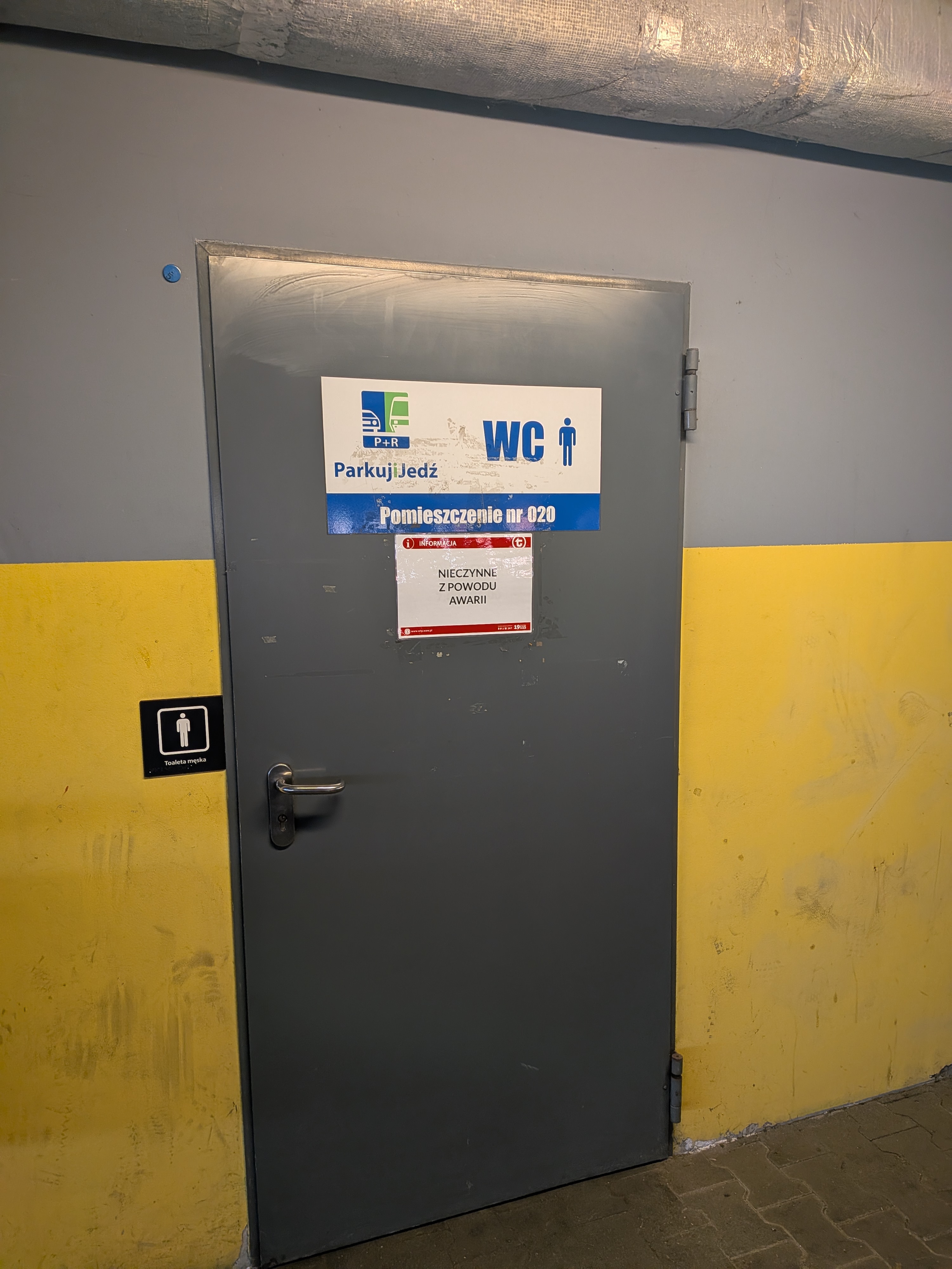 WC oznaczone jako toaleta męska w parkingu Parkuj i Jedź z wywieszoną karteczką że jest nieczynna 