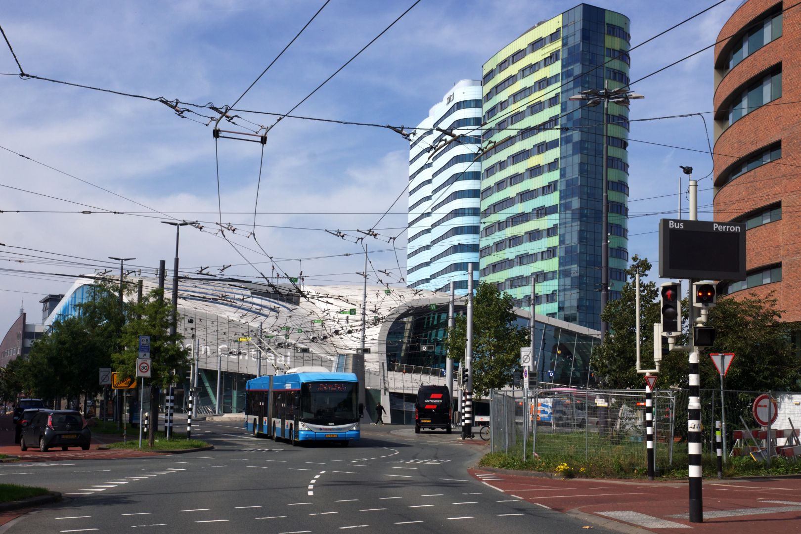 a blue and white trolleybus on a dedicated bus road between various very modern buildings, including the weirdly-shaped central station. Above the bus, a multitude of catenary junctions criss-cross the sky