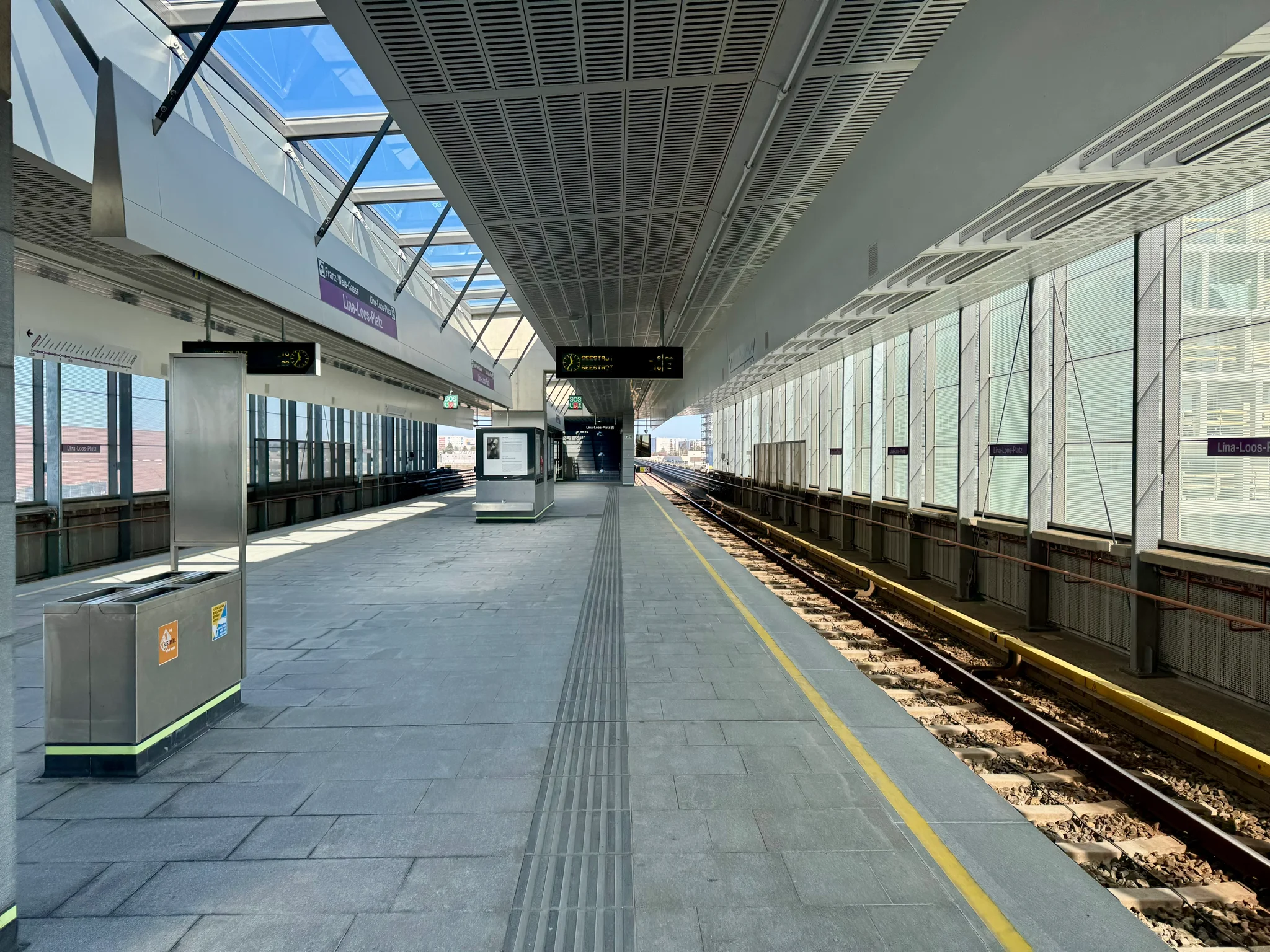 An ordinary above-ground Vienna U-Bahn station, with a wide island platform, fully encased platforms and tracks other than at the ends, and lots of glass.