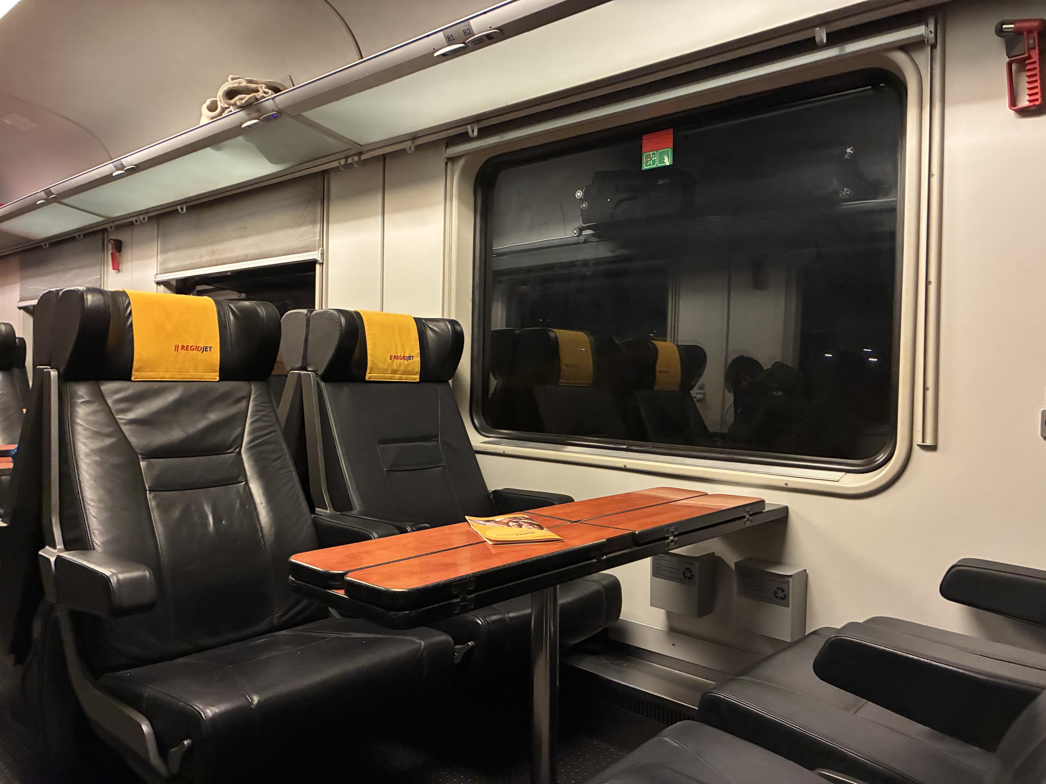 interior of the “relax” class train car of RegioJet, with comfy looking leather seats in a 2+1 arrangement, here pictured the 2s facing each other at a 4-person table