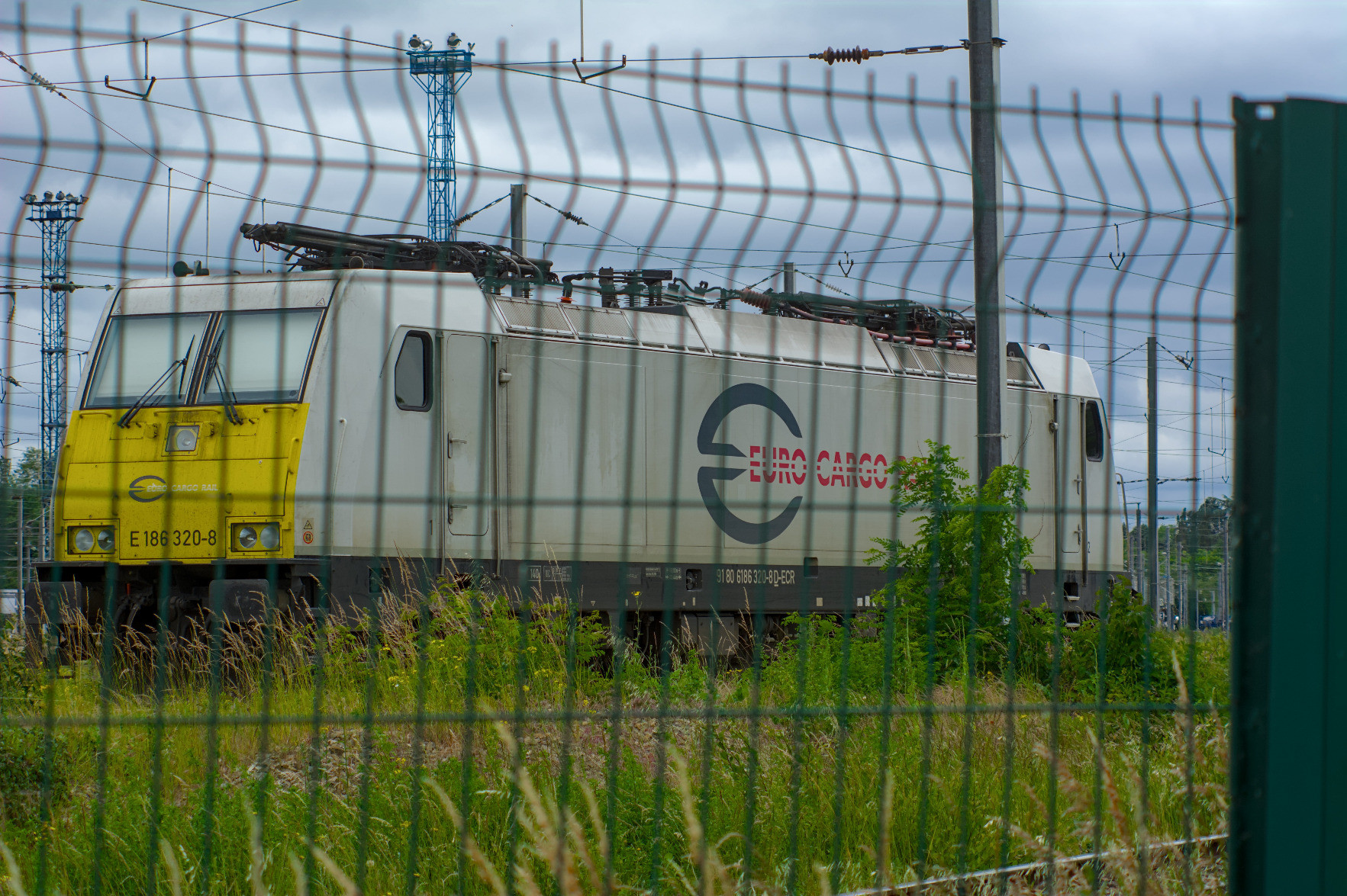 The yellow-nosed white Alstom Traxx locomotive parked, seen behind the fence. The yellow-nosed white Alstom Traxx locomotive parked, seen behind the fence.